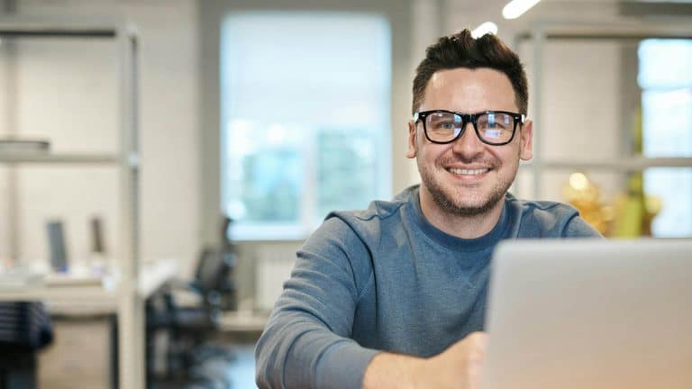 A happy man sits at his desk, smiling because he has completed the Highfield E-Learning Stress Management Course.