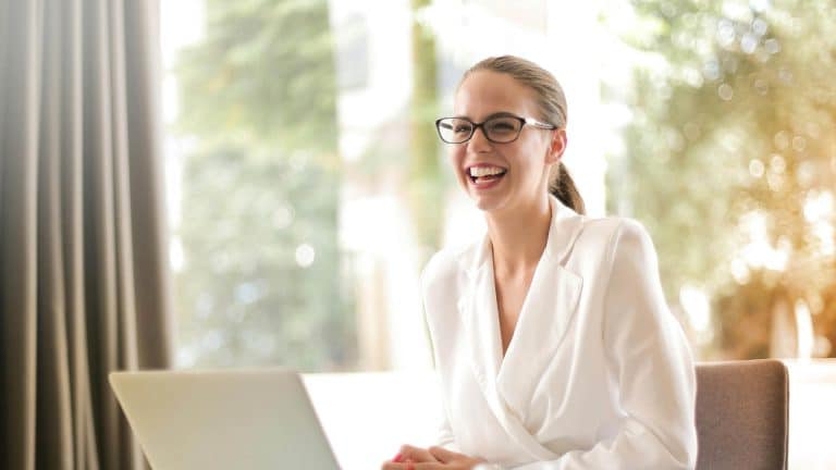 A woman in a white suit is smiling because she has completed her leadership and management course.