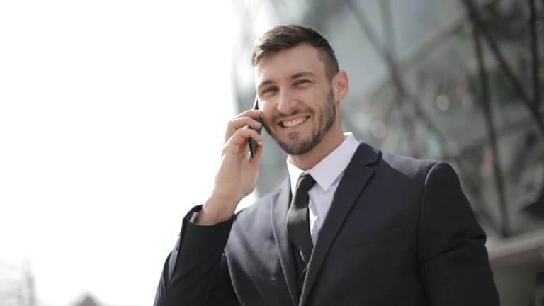 A man in a suit is confident and smiling while talking on the phone, thanks to his management and leadership course.