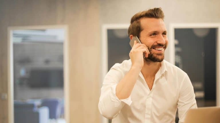 A man is smiling while talking on a smartphone, appearing confident after completing the Highfield E-Learning Communication Course.