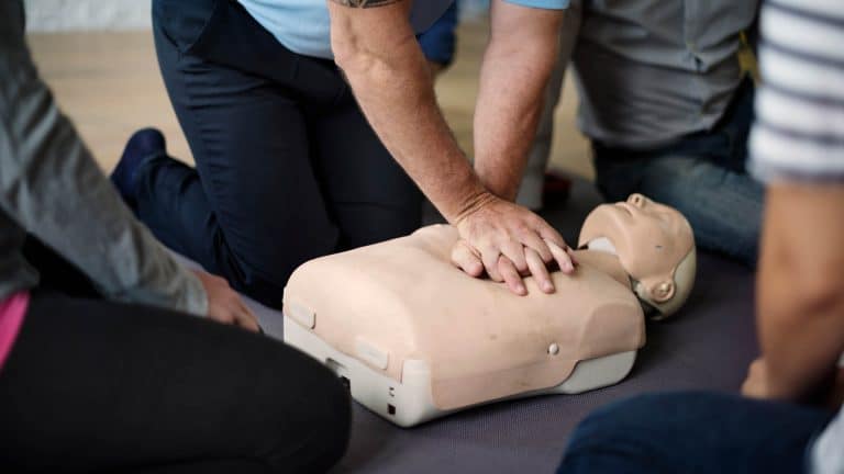 A trainer is demonstrating emergency CPR as part of the Highfield E-Learning Emergency First Aid Course.